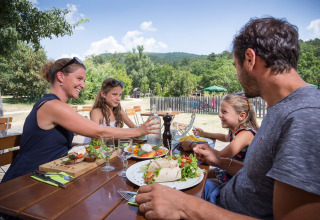 En familie nyder et måltid udendørs ved Village Huttopia Dieulefit feriested i Auvergne-Rhône-Alpes, Frankrig.
