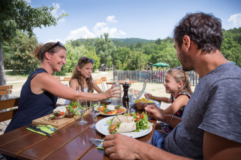 Une famille partage un repas en plein air au Village Huttopia Dieulefit, parc de vacances en Auvergne-Rhône-Alpes, France.
