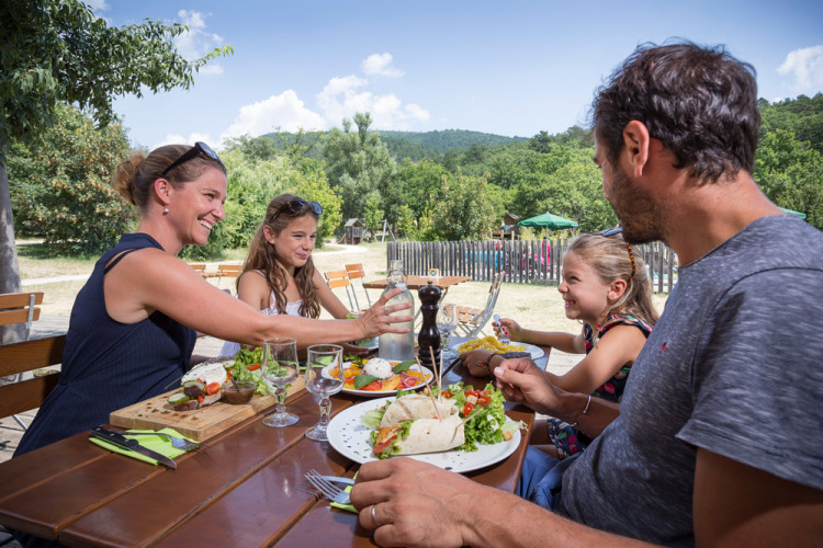 Familie genießt gemeinsam ein Mittagessen im Freien im Village Huttopia Dieulefit in Auvergne-Rhône-Alpes, Frankreich.