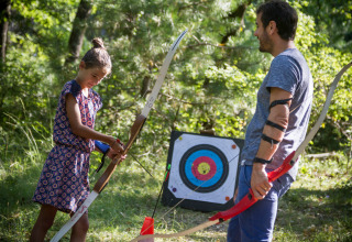 Barn og voksen lærer bueskydning ved en målskive i skoven på Village Huttopia Dieulefit, Frankrig.