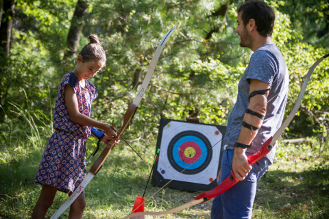 Ein Kind und ein Erwachsener üben Bogenschießen im Wald im Village Huttopia Dieulefit, Frankreich.