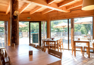 Træinteriør i restaurant ved Village Huttopia Dieulefit med udsigt til udendørs terrasse og parasoller.