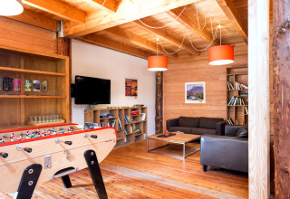 Sala luminosa con paredes de madera, futbolín, estanterías con libros y sofás en Huttopia Dieulefit.