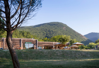 Modern wooden cabin with sun umbrellas in green mountain scenery at Village Huttopia Dieulefit, France.