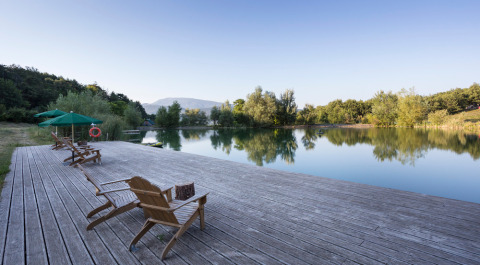 Vista apacible del lago con terraza de madera y tumbonas en el Village Huttopia Dieulefit, Auvergne-Rhône-Alpes, Francia.