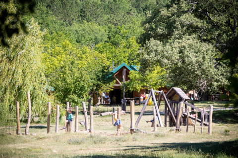 Niños jugando en un parque infantil natural rodeado de árboles en Village Huttopia Dieulefit, Auvergne-Rhône-Alpes.