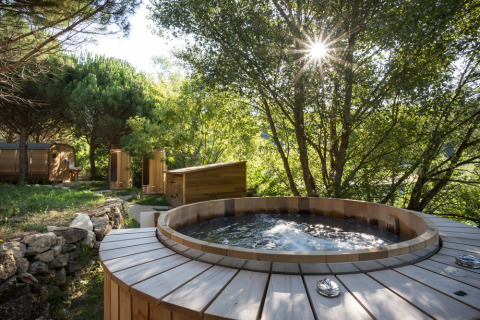 Bañera de hidromasaje de madera al aire libre rodeada de árboles en Village Huttopia Dieulefit, Auvernia-Ródano-Alpes, Francia.
