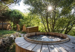Bain à remous extérieur en bois entouré de verdure au Village Huttopia Dieulefit, Auvergne-Rhône-Alpes, France.