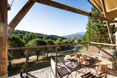 Desayuno en una terraza de madera con vistas a colinas y árboles en Village Huttopia Dieulefit, Francia.