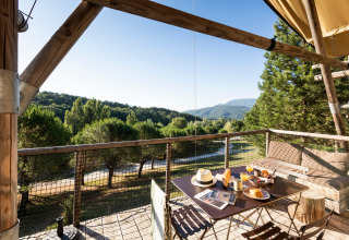 Ontbijt op een terras met uitzicht op groene heuvels in Village Huttopia Dieulefit, Auvergne-Rhône-Alpes.
