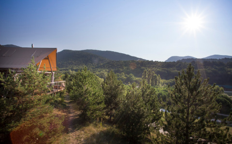 Paisaje soleado con pinos y colinas en el parque vacacional Village Huttopia Dieulefit en Auvergne-Rhône-Alpes, Francia.