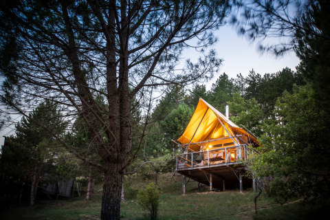 Verlichte hut op palen in het bos bij Village Huttopia Dieulefit, een vakantiepark in Auvergne-Rhône-Alpes, Frankrijk.