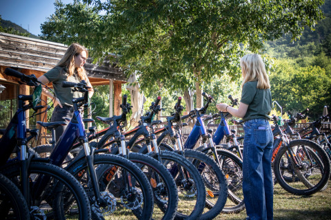 Two people selecting mountain bikes outdoors at Village Huttopia Dieulefit holiday park in France.