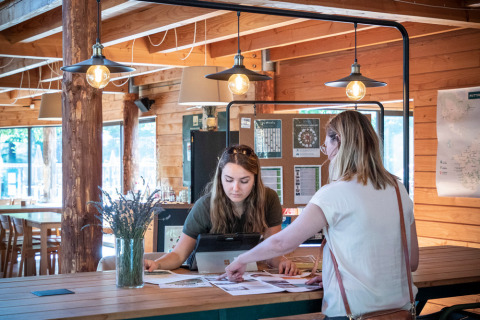 Twee vrouwen bekijken documenten aan een receptie in een houten gebouw in Village Huttopia Dieulefit, Frankrijk.