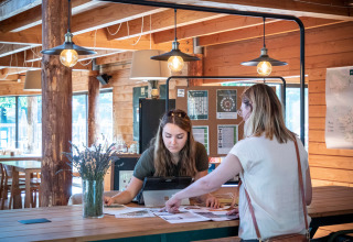 Twee vrouwen bekijken documenten aan een receptie in een houten gebouw in Village Huttopia Dieulefit, Frankrijk.