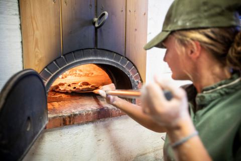 Persona horneando pizza en un horno de piedra en Village Huttopia Dieulefit, Auvernia-Ródano-Alpes, Francia.