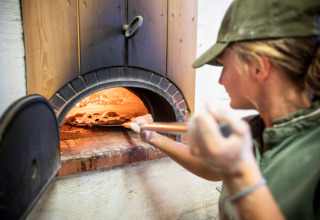Personne cuisant une pizza dans un four à bois au Village Huttopia Dieulefit, Auvergne-Rhône-Alpes, France.