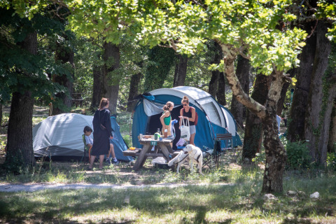 Persone in campeggio nei boschi al Village Huttopia Dieulefit, Auvergne-Rhône-Alpes, Francia, con tende e tavolo da picnic.