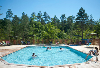 Udendørs swimmingpool med gæster, omgivet af skov ved Village Huttopia Lanmary, Nouvelle-Aquitaine, Frankrig.