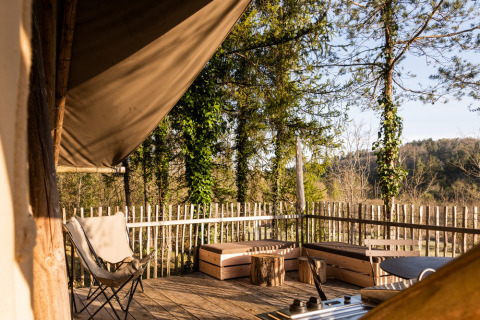 Terraza de madera soleada con sillas, bancos y valla rústica en Village Huttopia Lanmary, Nouvelle-Aquitaine.