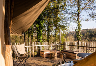 Sunny wooden terrace with chairs and benches surrounded by rustic fence and forest in Village Huttopia Lanmary.