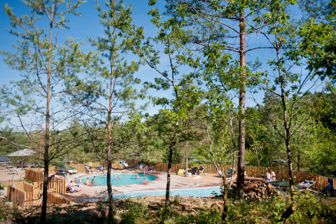 Zona de piscina al aire libre entre árboles en Village Huttopia Lanmary, un parque vacacional en Nouvelle-Aquitaine.