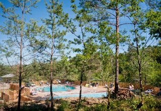 Piscine extérieure vue à travers les arbres au Village Huttopia Lanmary, parc de vacances en Nouvelle-Aquitaine.