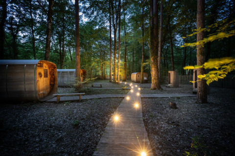 Cabañas de madera iluminadas y sendero forestal en Village Huttopia Lanmary, Nouvelle-Aquitania, Francia.