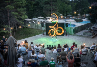 Pubblico assiste a uno spettacolo di fuoco su una terrazza in legno presso Village Huttopia Lanmary, Francia.