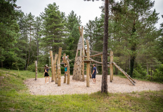 Børn og voksne leger på en naturlig legeplads i skoven ved Village Huttopia Lanmary, Nouvelle-Aquitaine.