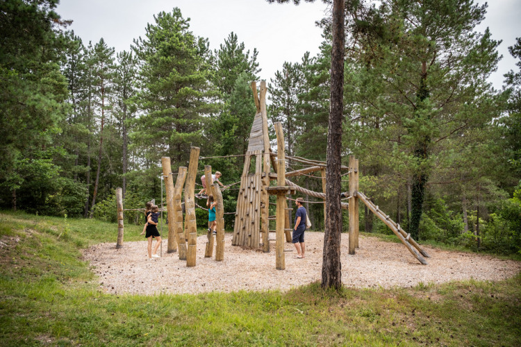 Enfants et adultes jouent sur une aire de jeux en bois à Village Huttopia Lanmary, en Nouvelle-Aquitaine, France.