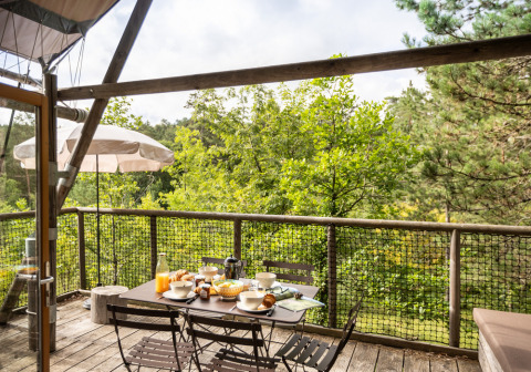 Terraza exterior con desayuno servido y vistas al bosque en Village Huttopia Lanmary, Nouvelle-Aquitaine, Francia.