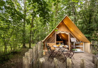 Trætelt med terrasse og udendørs spisebord, omgivet af skov ved Village Huttopia Lanmary i Frankrig.