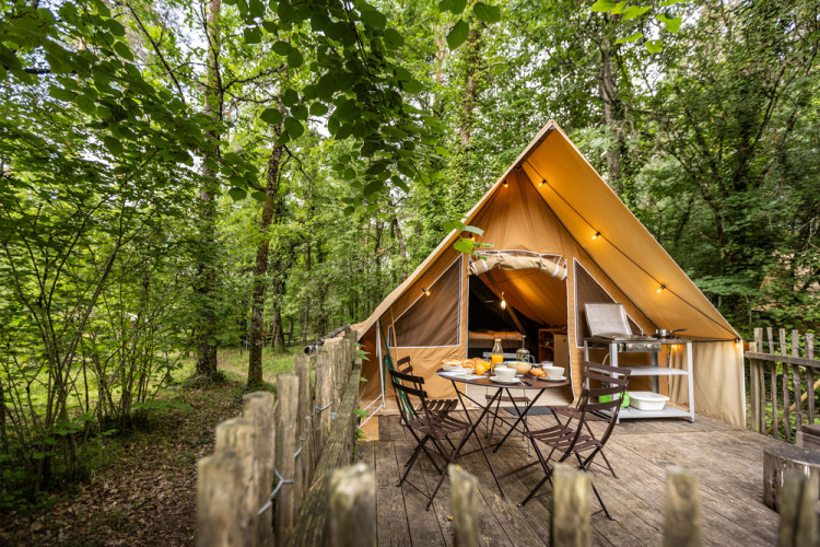 Tente glamping avec terrasse et table à manger extérieure dans la forêt à Village Huttopia Lanmary, France.