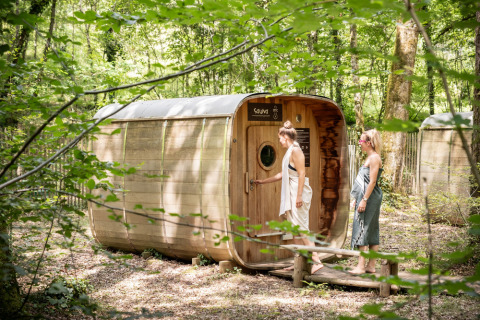 Dos mujeres se acercan a una sauna de madera en medio del bosque en Village Huttopia Lanmary, Francia.