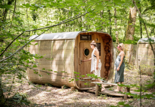 To kvinder nærmer sig en træsauna i skoven ved ferieparken Village Huttopia Lanmary i Frankrig.
