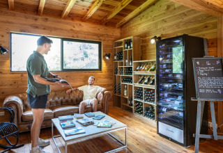 Two men in a cozy wooden lounge at Village Huttopia Lanmary, France, with wine racks in the background.