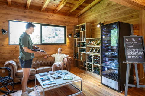 Two men in a cozy wooden lounge at Village Huttopia Lanmary, France, with wine racks in the background.