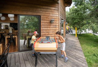 Twee kinderen spelen tafelvoetbal op een houten terras aan een chalet in vakantiepark Huttopia Lanmary, Frankrijk.