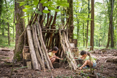 Dos niños juegan junto a una cabaña de troncos en el bosque de Village Huttopia Lanmary, Francia.