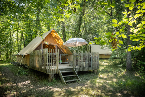 Una tienda de campaña glamping con terraza de madera en un bosque en Village Huttopia Lanmary, Nouvelle-Aquitaine, Francia.