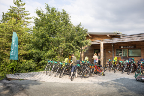 Alquiler de bicicletas frente a una cabaña de madera en Village Huttopia Lanmary, rodeado de árboles en Francia.