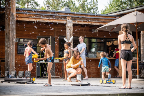 Kinderen spelen met bellen voor een houten chalet bij Village Huttopia Lanmary, Nouvelle-Aquitaine, Frankrijk.