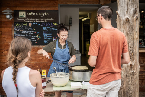 Een vrouw bakt crêpes bij Village Huttopia Lanmary terwijl bezoekers buiten voor het café wachten.