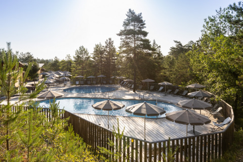 Piscina al aire libre rodeada de árboles y sombrillas en Village Huttopia Lanmary, Nouvelle-Aquitania, Francia.