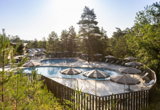 Swimmingpool med parasoller omgivet af træer på Village Huttopia Lanmary feriepark i Nouvelle-Aquitaine, Frankrig.