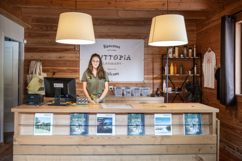 Área de recepción en Village Huttopia Lanmary, Nouvelle-Aquitania, Francia, con empleada tras el mostrador.