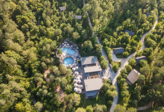 Luftfoto af Village Huttopia Lanmary feriepark i Nouvelle-Aquitaine, Frankrig, med pool og hytter i skoven.