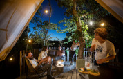 Cinque amici trascorrono una serata con cibo e bevande sulla terrazza di una tenda safari accogliente.