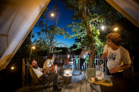 Fünf Freunde genießen einen entspannten Abend mit Essen und Getränken auf der Terrasse eines Safarizelts.
